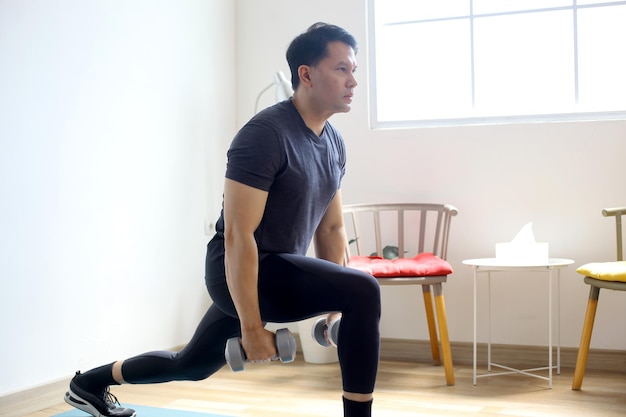 Portrait of Asian sporty man doing dumbbells workout at home working on arms strength