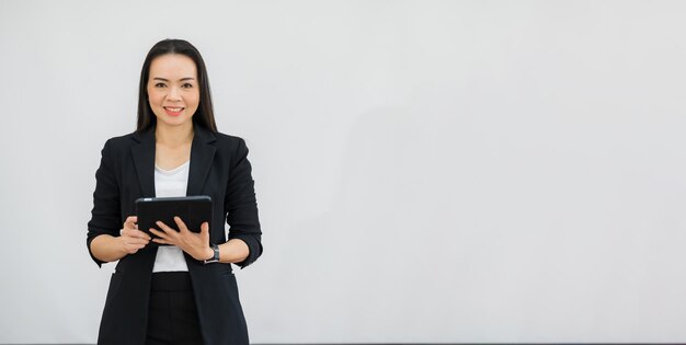 Portrait of an Asian teacher holding a tablet in front of an empty classroom at university.isolated background