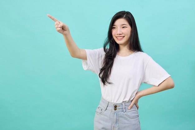 Портрет азиатского подростка, красивой молодой женщины, улыбающейся, смеющейся, указывающей пальцем в сторону от пустого пространства для копирования