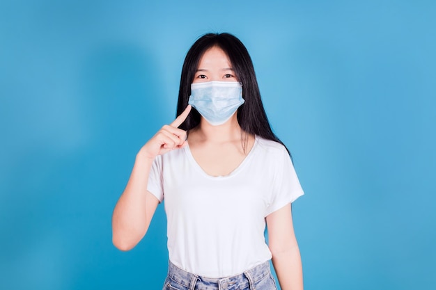 Portrait of asian teenager wearing and pointing a medical face mask to protect Covid19 Coronavirus on blue background