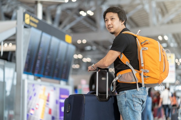 Portrait of Asian traveler with luggage with passport standing over the flight board for c