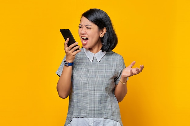Portrait of asian woman angry when talk at smartphone over yellow background