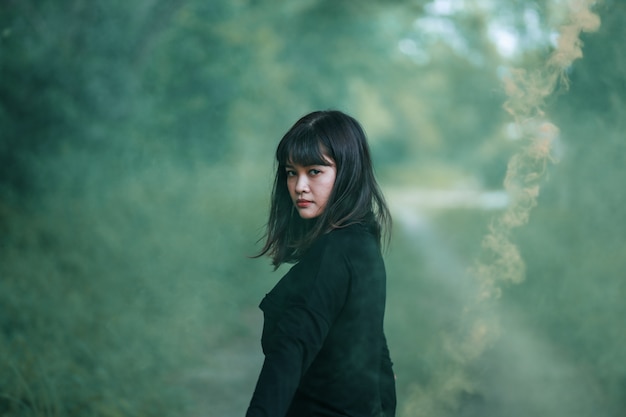 Portrait of Asian woman in black cloth with color fire smoke in forest witch concept