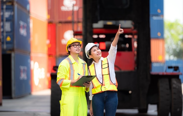 Portrait of Asian woman engineer and worker working with coworker at overseas shipping container