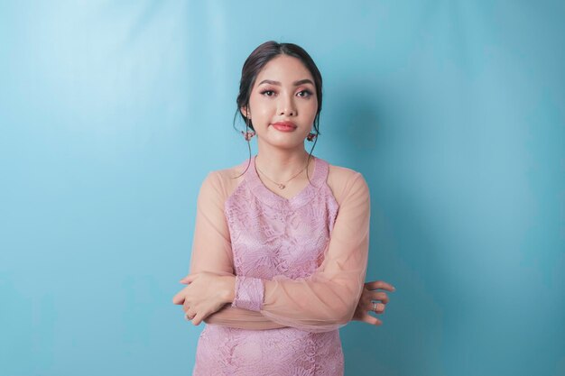 A portrait of asian woman folding her arms looks upset wearing modern kebaya isolated by blue background