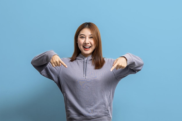 Portrait of Asian woman gesturing pointing at empty space for ad text portrait concept used for advertisement and signage isolated over blue background copy space