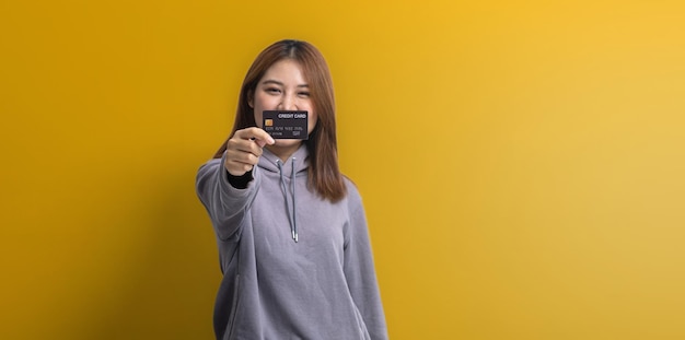 Portrait of Asian woman holding a credit card credit card spending concept online payment and general store with credit card isolated over yellow background copy space