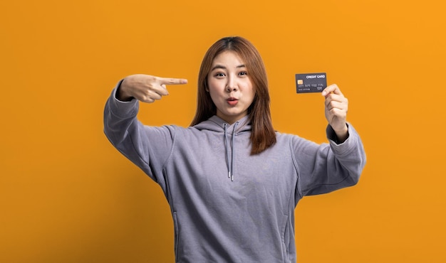 Photo portrait of asian woman holding a credit card credit card spending concept online payment and general store with credit card isolated over yellow background copy space