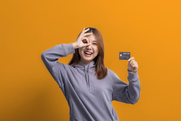 Portrait of Asian woman holding a credit card credit card spending concept online payment and general store with credit card isolated over yellow background copy space