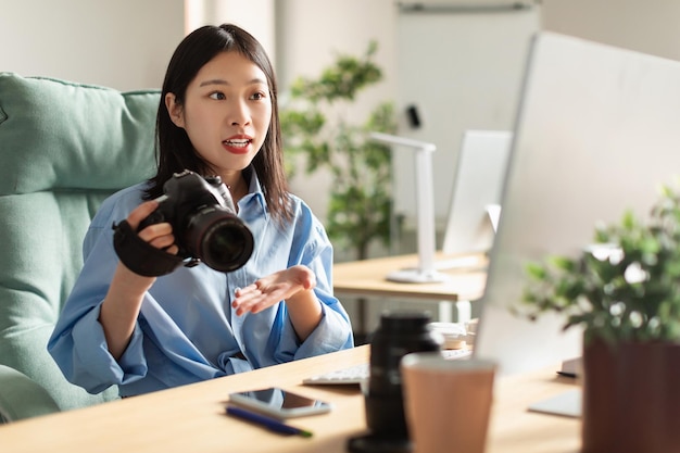 Ritratto della donna asiatica che tiene la macchina fotografica della foto che esamina il computer portatile