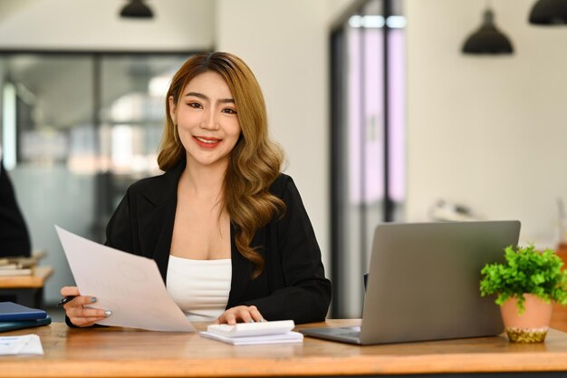 Photo portrait of asian woman investor using laptop and working on financial document in office