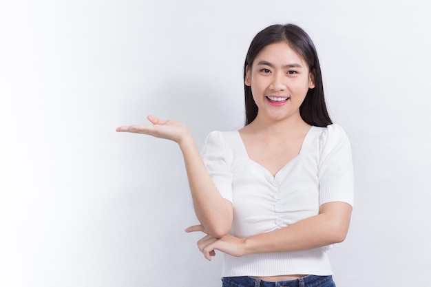 La donna asiatica del ritratto sta sorridendo e mostra le sue mani per presentare qualcosa sullo sfondo bianco.