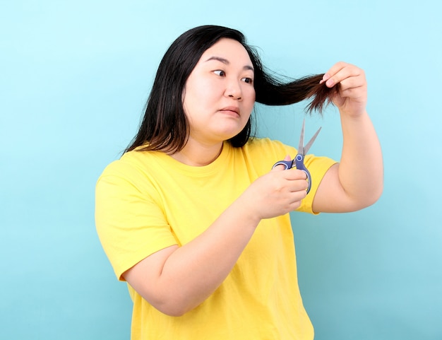 Portrait Asian woman wants to cut her damaged hair,on blue background in studio.