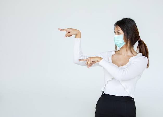 Portrait Asian woman wearing a face mask poses, pointing advertisement on white background, blank copy space with isolated white background cutout.