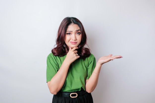 A portrait of an Asian woman wearing a green tshirt looks so confused isolated by a white background