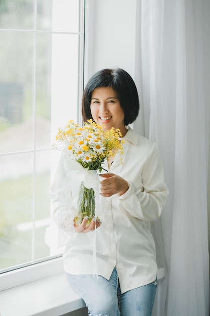 집 창가에 야생화 꽃다발을 들고 있는 아시아 여성의 초상화
