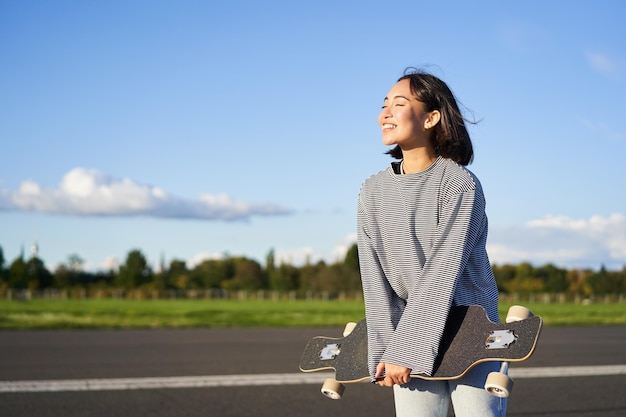 Portrait of asian woman with longboard korean girl skating holding skateboard in hands posing on roa