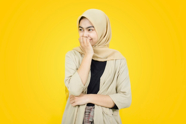 Photo portrait of asian women bites her fingers and looking away on yellow wall