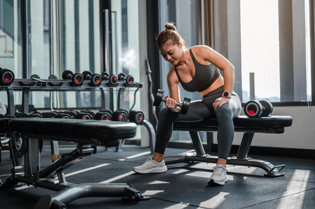 Photo portrait of asian women in sportswear working out with weights over exercise bench exercising are li