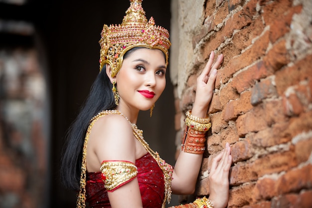 Portrait of an Asian Women in Thai Traditional dancer Clothes are Standing Against Ancient buddha statue. Ayuttaya Historical Park, Thailand Asia.