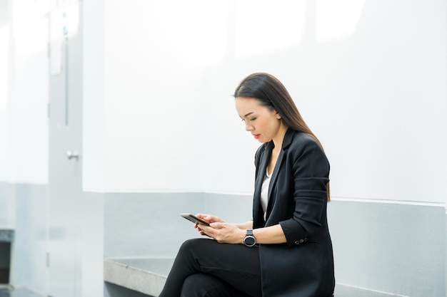 Ritratto di una donna lavoratrice asiatica che indossa un abito nero con in mano un telefono cellulare connesso a internet per inviare informazioni sul lavoro. concetto di utilizzo della tecnologia internet nella vita quotidiana