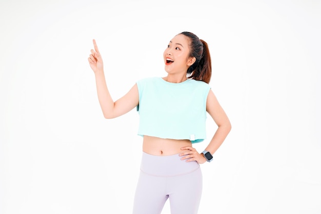 Portrait of Asian young beautiful and cheerful woman in gym workout outfit with finger point on copy space isolated on background