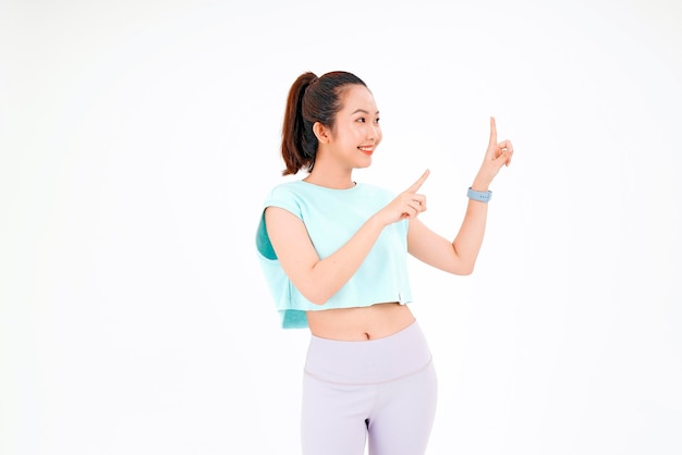 Portrait of Asian young beautiful and cheerful woman in gym workout outfit with finger point on copy space isolated on background