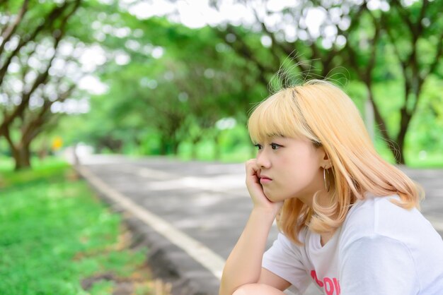 Ritratto di giovane ragazza asiatica sedersi al tunnel alberi bella donna tailandese scatta una foto all'apertoconcetto di donna triste che pensa dall'amoreil cuore spezzato dal fidanzato