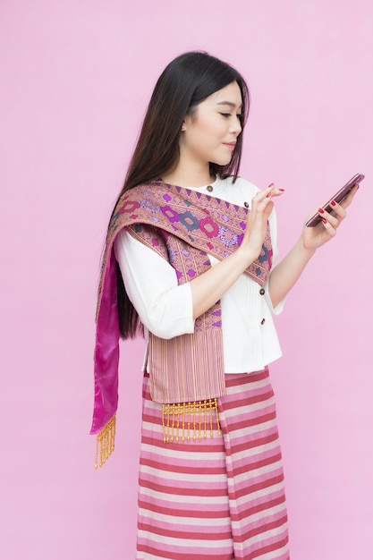 伝統的なタイのドレスでアジアの若い女の子の肖像画とピンクの背中にスマートフォンを持って