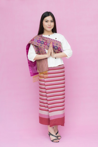 Portrait of asian young girl in traditional thai dress praying isolated on pink background