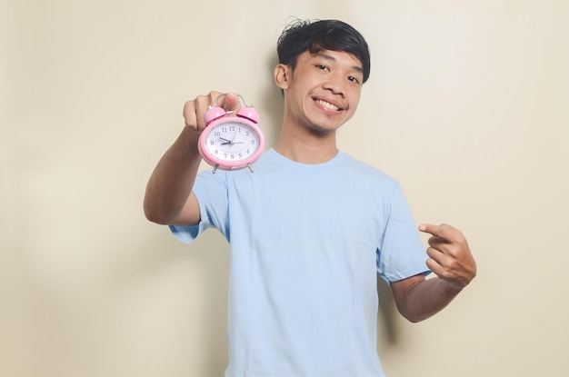 Portrait of asian young man showing alarm clock on isolated background