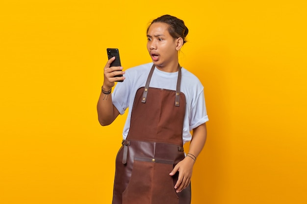 Portrait of asian young man wearing apron surprised to see incoming message on smartphone