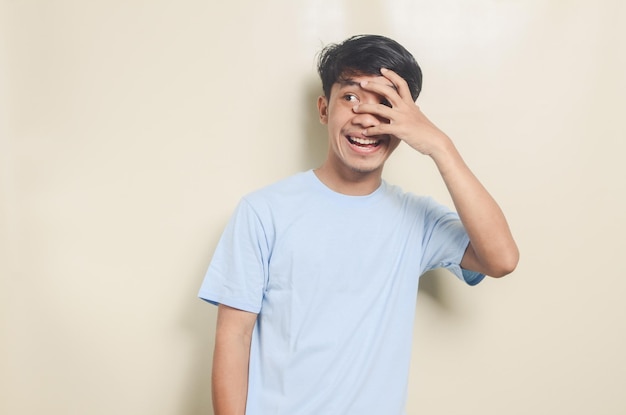 Портрет азиатского молодого человека в синей футболке, смотрящего одним глазом на изолированный фон