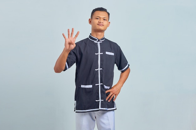 Portrait of Asian young man wearing karate making number four sign with finger over gray background