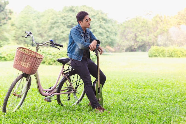 自転車に乗っている肖像画のアジアの若い男性ギター