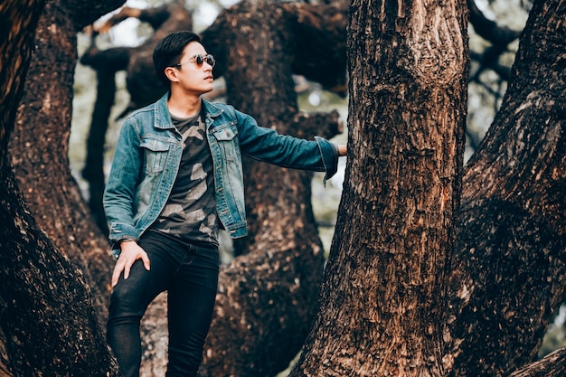 Портрет азиатских молодых людей носить солнцезащитные очки и джинсы рубашки, стоя на дереве