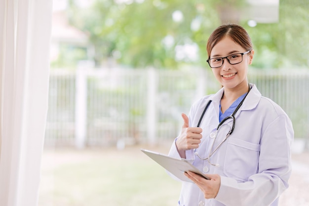 Portrait asian young teen medical staff doctor physician thumbs up with green nature blur background copy space