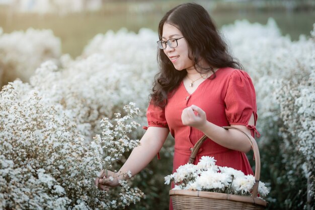 白い花で楽しむ赤いドレスとアジアの若い女性の幸せな旅行者の肖像画またはチェンマイ、タイの自然庭園で白いマルガリータの花畑、旅行リラックス休暇の概念