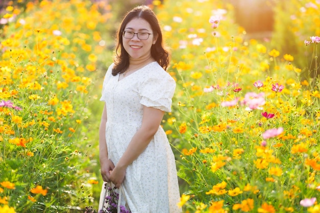 Portrait of asian Young woman happy traveler with white dress enjoying in Yellow and pink sulfur Cosmos flowers blooming field in the nature garden of in Chiang MaiThailandtravel relax vacation