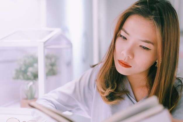 Portrait of asian young woman reading book on windowsill at home