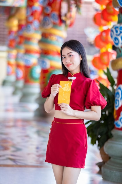 Portrait asian young woman wearing red traditional chinese\
cheongsam decoration holding yellow angpao envelopes with the\
chinese text blessings written on it is a good luck for happy\
chinese new year