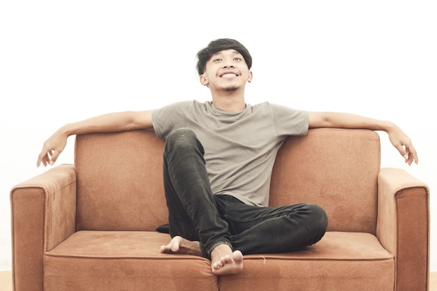 Portrait of asian youth wearing gray t-shirt sitting on the sofa laughing happily