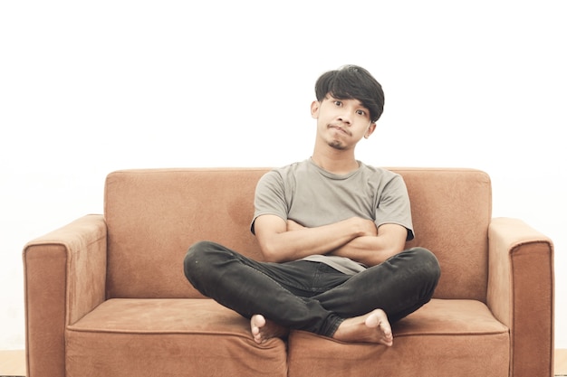 Portrait of asian youth wearing gray t-shirt sitting on the sofa thinking