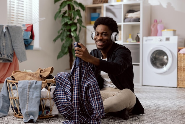 Ritratto di giovani sorridenti che piegano vestiti puliti che smistano il bucato prima di metterlo in lavatrice uno studente seduto sul pavimento del bagno ascoltando musica con le cuffie wireless