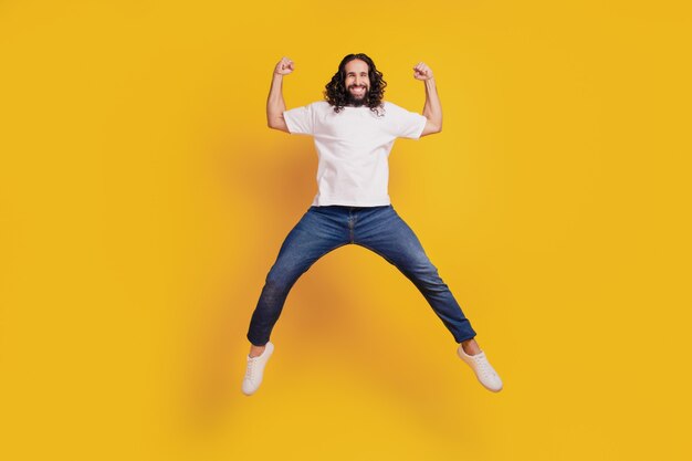 Portrait of astonished excited active guy jump hold fists on yellow background