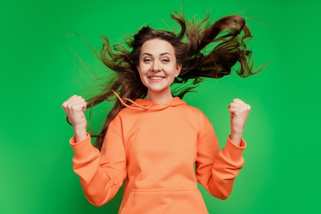 Portrait of astonished excited lady raise fists wind blow hairdo on green background