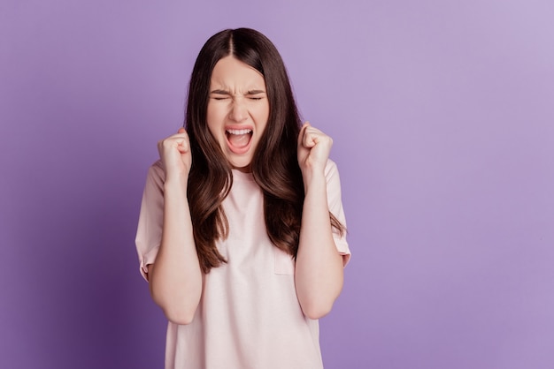 Portrait of astonished winner woman raise fists scream isolated on violet background
