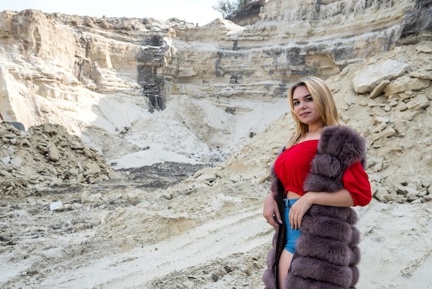 Portrait of astonishing young woman wearing fur coat in dry empty sand quarry