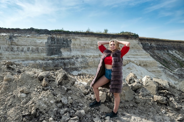 Portrait of astonishing young woman wearing fur coat in dry empty sand quarry