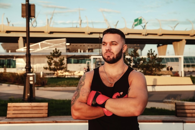 Portrait athletes man boxer fighter with boxing gloves posing with arms and biceps and looking away at urban background